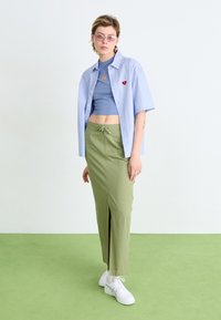Svetlomodrá krátka košeľa s červeným srdcovým detailom, sivý crop top, olivovo zelená maxi sukňa s predným rozparkom a biele tenisky.