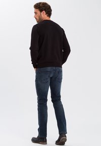 Czarny sweter, okrągły dekolt, prążkowane mankiety i dół, w połączeniu z ciemnoniebieskimi dżinsami, które mają kieszenie i prosty krój nogawek, dopełnione czarnymi botkami.