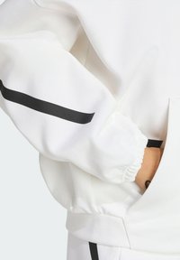 White sweatshirt with black accent stripe along the sleeve and elasticated cuffs. Features a kangaroo pocket for storage. Smooth texture.
