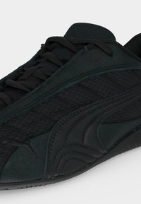 Gros plan d'une basket noire avec tissu texturé et détails en cuir, avec des lacets et un design courbé sur le côté.
