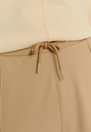 Béžová mikina s hladkým povrchom, s predným švom a šnúrkovým uzatváraním. Hroty šnúrky sú valcovité a mäkké, v zodpovedajúcej farbe.