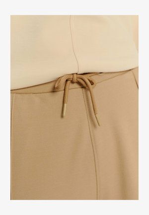 Béžová mikina s hladkým povrchom, s predným švom a šnúrkovým uzatváraním. Hroty šnúrky sú valcovité a mäkké, v zodpovedajúcej farbe.