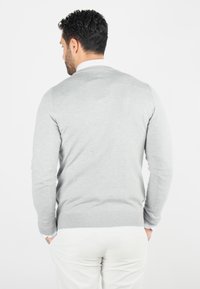 Pull en maille gris avec des manches longues, un col rond et une coupe ajustée, associé à un pantalon de couleur claire. Texture lisse avec un minimum de détails.