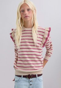 Suéter de rayas beige con líneas fucsias, con mangas rizadas y puños acanalados. Combinado con jeans de cintura alta en azul claro y un cinturón marrón.