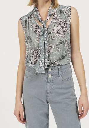 Blouse sans manches à motif floral avec col à nouer en vert grisâtre associée à un jean taille haute gris clair avec fermeture à boutons.