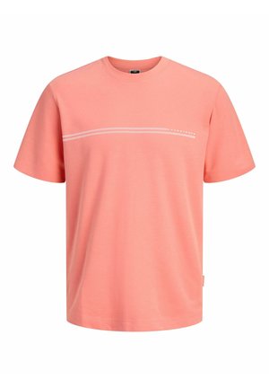 Chłopiec stoi i uśmiecha się, ubrany w koralową koszulkę z krótkim rękawem na białych długich rękawach, oliwkowe szorty typu cargo, białe skarpetki i czarno-białe sportowe buty.