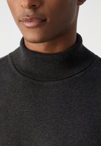 Rullekrave sweater i mørk grå strikket stof, med ribbet tekstur og høj krave, som giver en tætsiddende pasform omkring halsen og skuldrene.