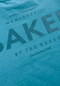 Türkise puuvillane T-särk, millel on suur graafiline tekst "BAKER" kulunud viimistlusega ja väiksemad tekstielemendid kontrastse tumeda värviga.