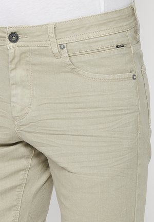 Pantaloni dintr-un amestec de bumbac bej cu un croi slim, prevăzuți cu un sistem de închidere cu nasture, un design clasic cu cinci buzunare și detalii de cusătură discrete.