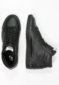 Svarta läder högtopps sneakers med texturerad yta, svarta snören och vita sula accenter. Har en Nike-logotyp på tungan.