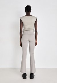 Gray fitted top with short sleeves and high-waisted light gray flared pants, paired with black shoes, viewed from the back.