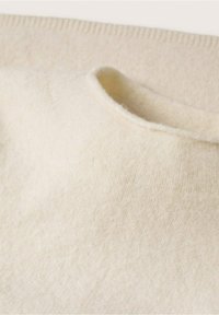 Pull en laine couleur crème avec un col rond, une texture douce et des détails en côtes au niveau du col.