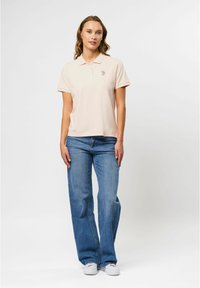  Lichtroze polo met een kraag en korte mouwen, voorzien van een klein logo. Gecombineerd met blauwe rechte jeans en witte sneakers.