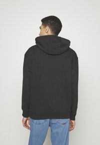 Sudadera negra con capucha de textura suave, puños acanalados y un ajuste casual, combinada con jeans de color azul claro.