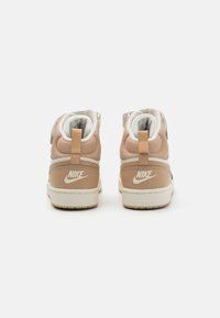 Sapatilhas de cano alto da Nike em bege e branco, com parte superior em malha, detalhes em couro texturizado e uma alça na parte traseira.