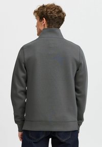 Grey pullover sweatshirt with a high collar, smooth texture, and ribbed hem, paired with dark denim jeans. Back view.