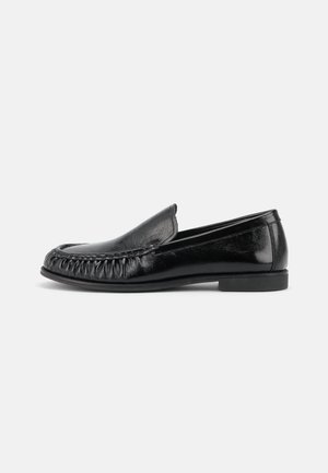 Mocassino in pelle nera slip-on con punta arrotondata, dettagli cuciti sulla parte anteriore e tacco basso e piatto, mostrato di profilo.