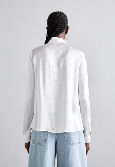 Hvid silke skjorte med stjernemønster, lange ærmer og krave. Sammen med lyseblå denim, der har en afslappet pasform og slids på bagsiden.