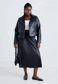 Črna jakna iz umetnega usnja, bela kratka majica, črna plisirana midi krila in črne balerinke, dopolnjene s črno torbico.