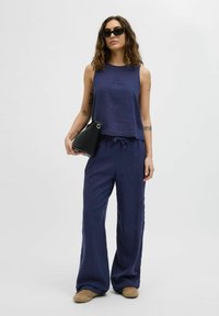 Marineblauwe linnen mouwloze top en bijpassende wijde broek met eenkoord in de taille. Een zwarte driehoekige clutch en zonnebril maken de look compleet.