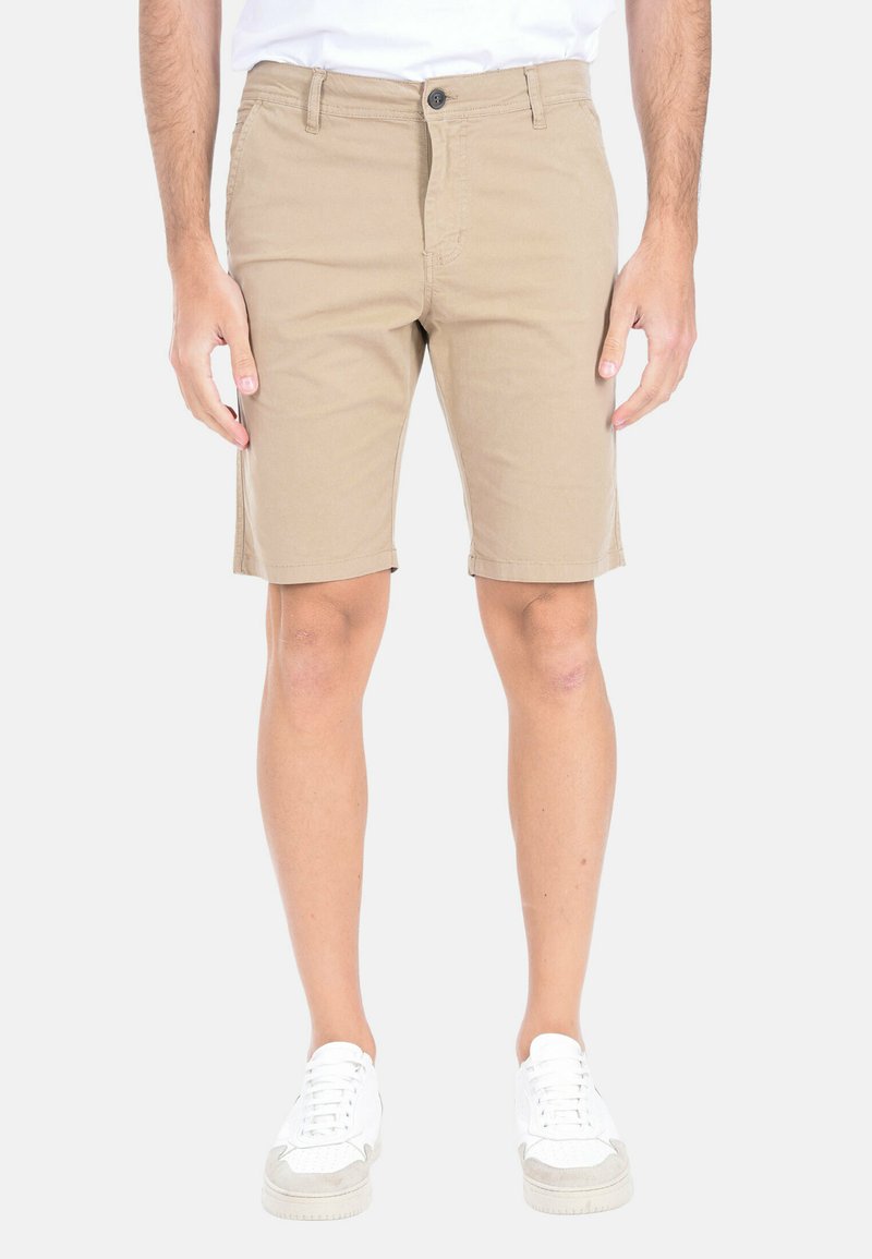 Shorts beige in cotone con taglio dritto e tasche frontali, chiusura con bottone e una superficie liscia, indossati con sneakers bianche.