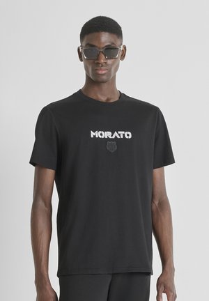 Camiseta negra de algodón, presenta el logo "MORATO" en blanco con un emblema texturizado en negro debajo, cuello redondo, mangas cortas, corte relajado.