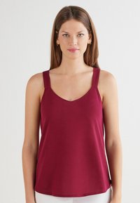 Burgunderrotes ärmelloses Oberteil mit V-Ausschnitt und breiten Schulterträgern. Glatter Stoff mit legerer Passform und dezenten Nahtdetails.