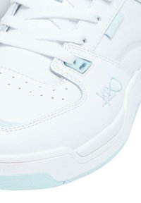 Hvit sneaker med en glatt skinnoverdel, lyseblå detaljer, perforert tåboks og flate hvite snøringer. Har en teksturert såle.