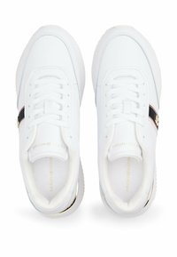 Un paio di sneakers bianche con lacci, strisce laterali nere e rosse e dettagli del logo in tono oro visti dall'alto.