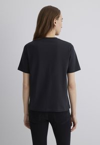 Black short-sleeve T-shirt viewed from the back. Features a crew neck and a straight hemline. Fabric appears soft with a smooth texture.