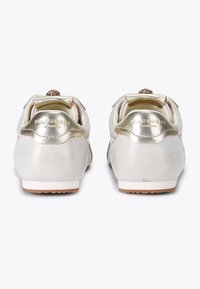 Metallische zilveren sneakers met een gladde textuur, voorzien van gouden accenten en decoratieve hardware op de achterkant. Duidelijke branding zichtbaar.