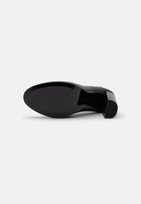 Scarpa nera con tacco alto, dalla tomaia liscia e lucida e dal tacco testurizzato. La suola è piatta e leggermente sagomata per il comfort.