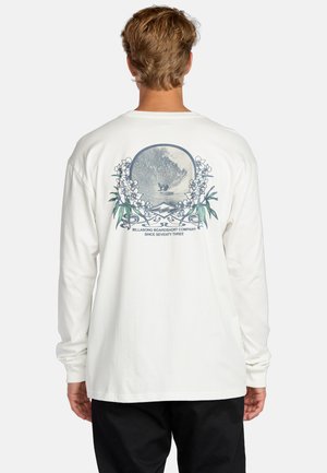 Witte longsleeve shirt met een grafisch ontwerp van een golf omringd door bloem elementen en tekst, gemaakt van zachte katoenen stof.