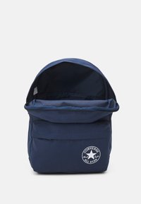Mochila de color azul marino hecha de tela duradera, con una tapa plegable, un bolsillo frontal y un logotipo blanco de "Converse All Star".