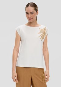 Haut blanc à manches courtes avec un col rond et des d�étails de broderie en feuille d'or sur le côté gauche. Tissu lisse avec une coupe décontractée.
