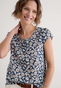 Námořnická blůza s bílým a oranžovým potiskem sedmikrásek, kulatým výstřihem, krátkými nabíranými rukávy, lehkým materiálem a uvolněným střihem.