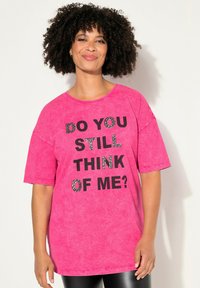 Helles pinkes Übergröße-T-Shirt mit kurzen Ärmeln und rundem Halsausschnitt. Schwarzer Text mit der Aufschrift "DENKST DU NOCH AN MICH?" mit Strassakzenten.