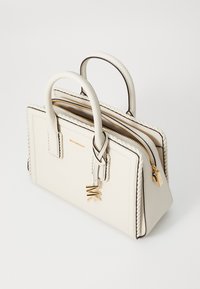 Strukturiertes weißes Lederhandtasche mit zwei Griffen, verziert mit einem geflochtenen Akzent, goldfarbenen Reißverschlüssen und einem daran befestigten Charme.