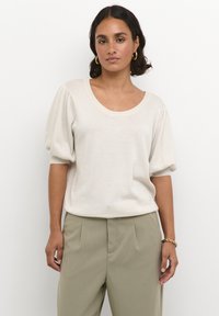 Hellbeige Kurzarmoberteil mit Rundhalsausschnitt, Puffärmeln und weicher Textur, kombiniert mit olivgrünen Hosen. Einfaches Design, keine Muster.