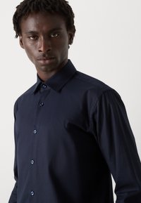 Camisa azul marino de botones con cuello estructurado, que presenta una tela texturizada y botones a juego en el frente.