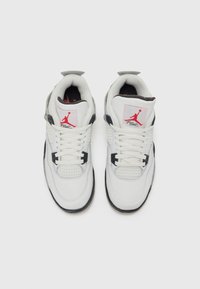 Biele tenisky s sieťovinovým prstom, čiernymi akcentmi, polstrovaným golierom a červeným logom Jumpman na jazyku. Obsahujú ploché šnúrky a gumovú podrážku.