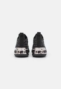 Schwarze Sportschuhe mit einer strukturierten Oberseite, die mit schwarzen Nieten und einem glänzenden silbernen Fersenakzent mit der Aufschrift "KARL" versehen sind.