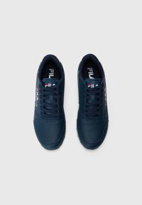 Mørk marineblå sneakers med en glatt skinnoverflate, snøring, perforert tåområde og merkevaredetaljer i hvitt og rødt.