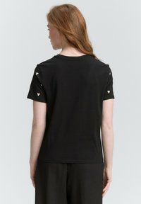 Czarny t-shirt z krótkim rękawem, ozdobiony białymi akcentami w kształcie serca przy rękawach. Gładki, lekki materiał i klasyczny okrągły dekolt.