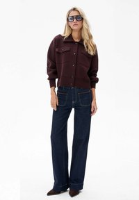 Bordowy sweter na guziki z kołnierzem, zestawiony z szerokimi ciemnoniebieskimi dżinsami i brązowymi butami w szpic.