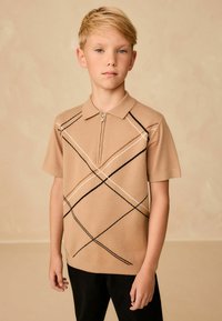 Beige lühikese varrukaga polo särk, millel on tõmbluku krae, mustade ja valgete diagonaalliinidega ning tekstuuriga kudumismuster. Kanda mustade pükstega.
