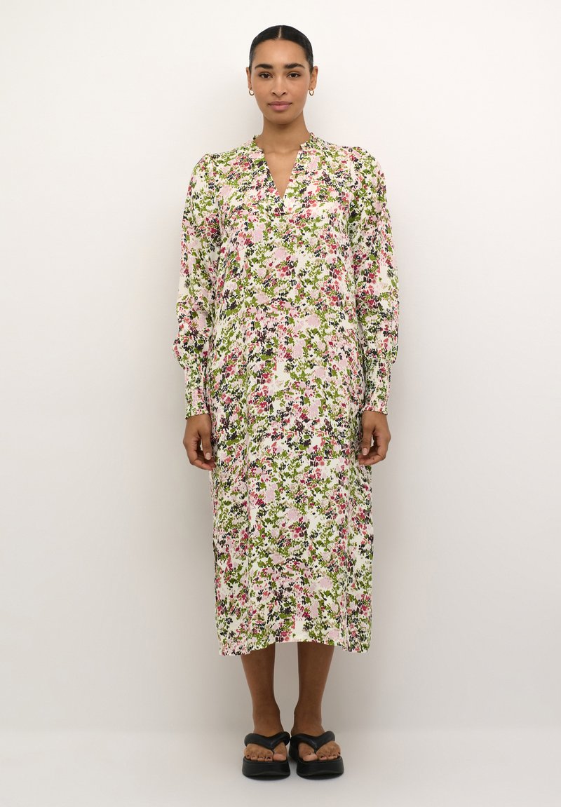 Robe florale présentant un mélange de motifs roses, verts et noirs sur un fond blanc. Manches longues et décolleté en V, silhouette fluide.