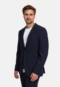 Blazer blu Navy, tessuto testurizzato, chiusura a un bottone, due tasche frontali, rever a punta, abbinato a una maglietta bianca sottostante.