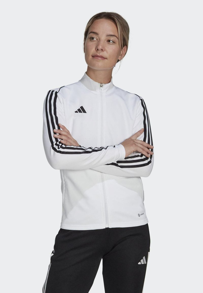 Weißer Zip-Jacke mit schwarzen Streifen an den Ärmeln, mit hohem Kragen und dem Adidas-Logo auf der linken Brust. Weiches, sportliches Material.