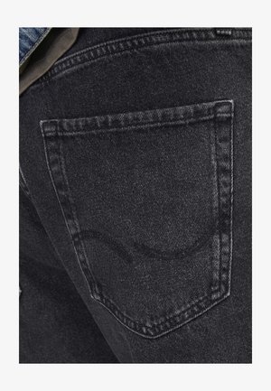 Jeans de denim preto com um bolso traseiro com detalhes de costura subtil. A textura é ligeiramente gasta, com um acabamento suave e desbotado.